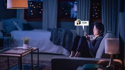 A teenage girl browsing social media late at night. The post she is looking at has been viewed 723,000 times.