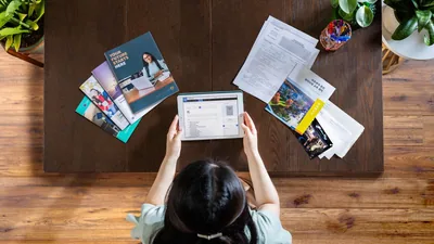 A young sister using a tablet to do research on possible future goals. To her left are brochures about secular education. To her right is an application for expanded theocratic service and information about Bethel.