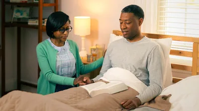 An ill brother sitting up in bed and praying with his wife.