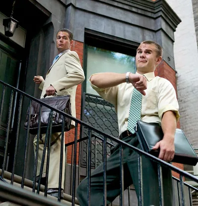 A brother impatiently checking his watch while in field service. His witnessing partner glances at him.